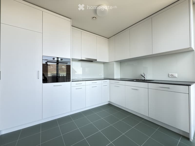 Modern kitchen with white cabinets, dark grey tiled floor, stainless steel sink, and built-in oven.