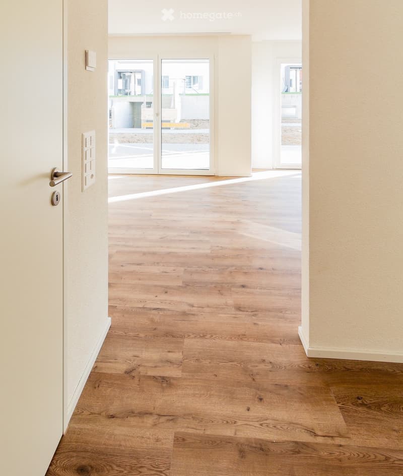 Empty hallway with light wooden flooring, white walls, and a sliding glass door leading outside.