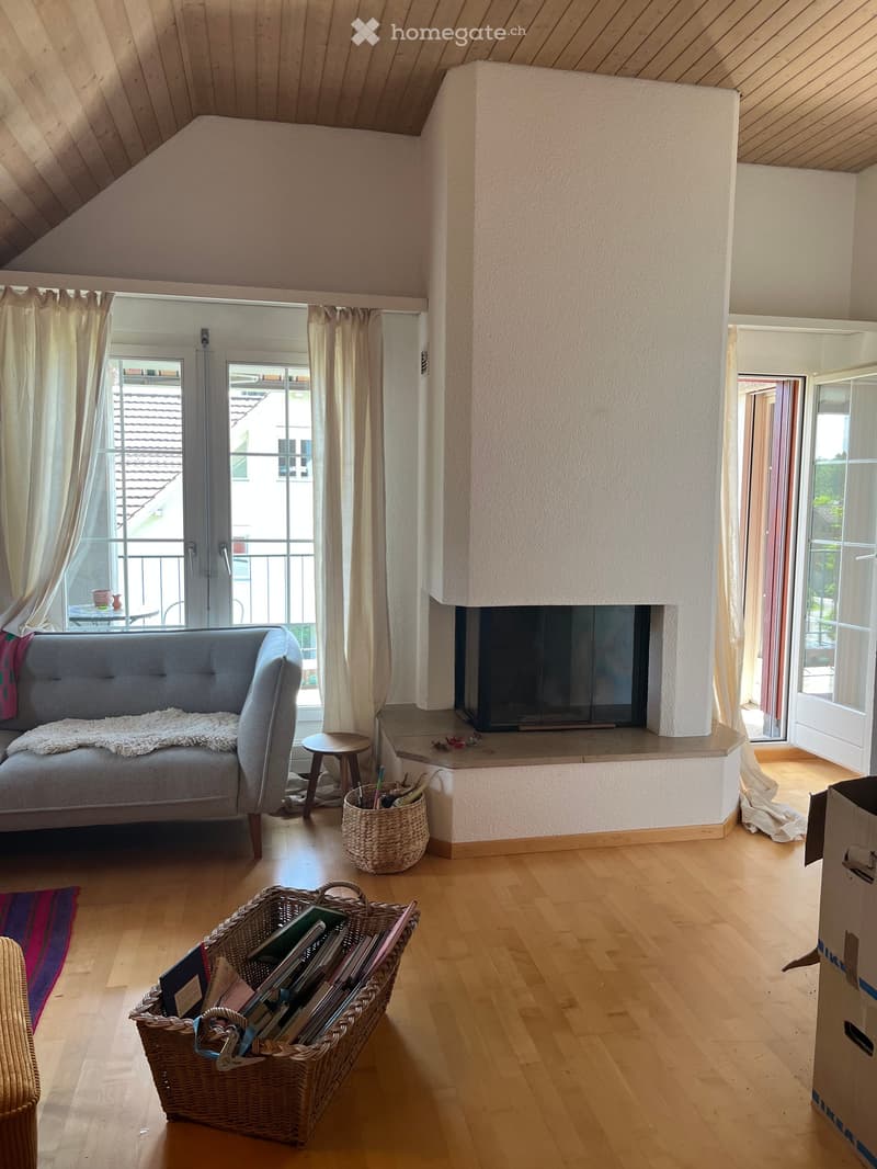 Living room with wooden flooring, fireplace, grey sofa, small wooden stool, wicker baskets, and a balcony with a view.