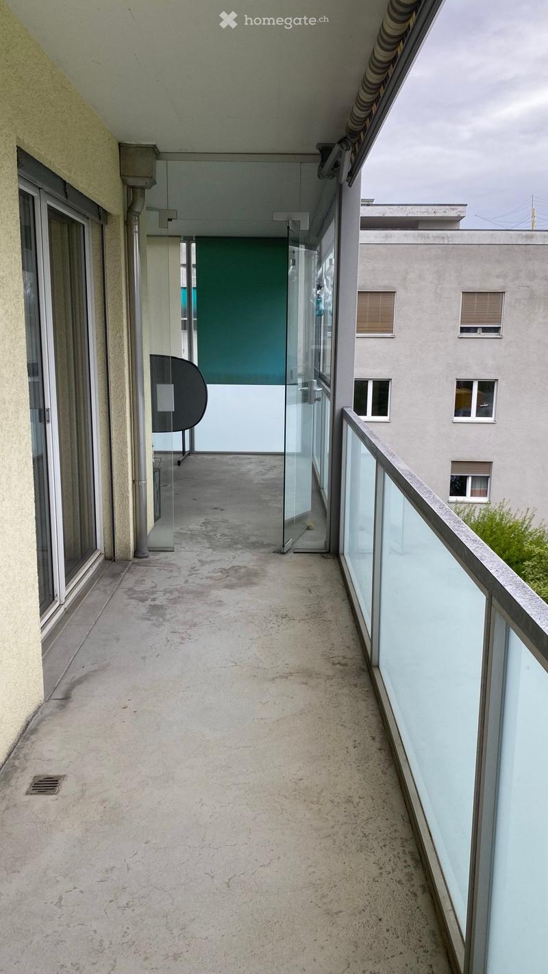 Empty balcony with concrete floor, glass railings, and a glass door leading to an interior space.