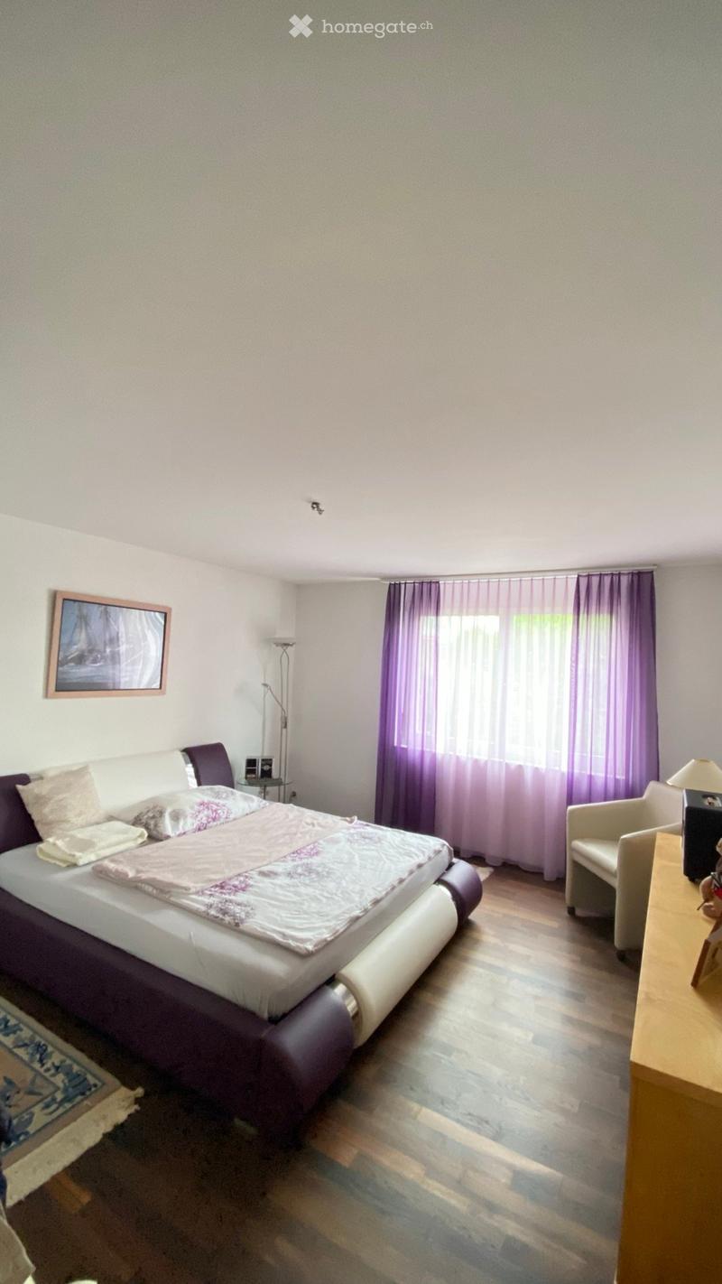 Modern bedroom with a large bed, white and purple bedding, a wooden floor, a chair, a small table, and a picture frame on the wall.