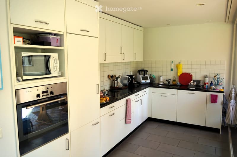 Modern kitchen with white cabinets, stainless steel appliances, and black countertops. Features include a microwave, oven, sink, and various kitchen utensils.