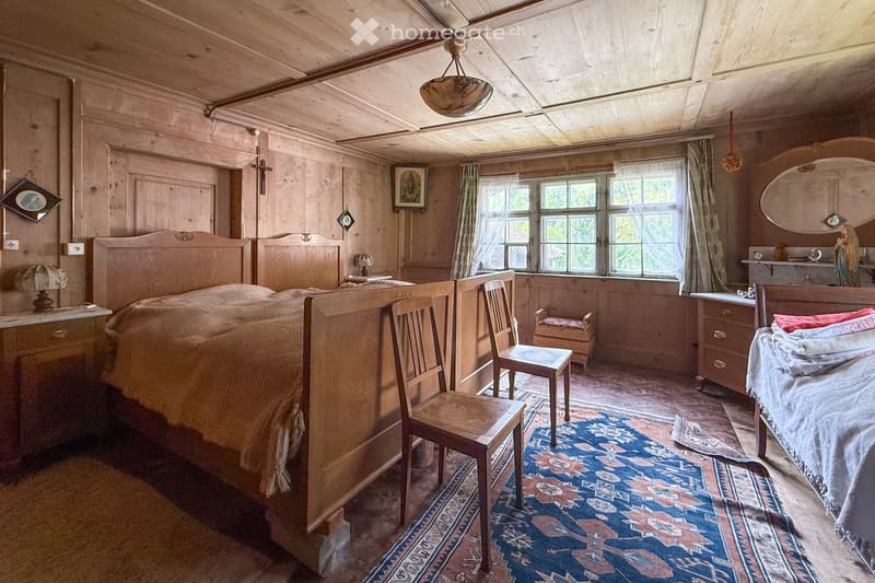 Bedroom with wooden beds, wooden walls and flooring, large windows, wooden chairs, rug, nightstand, lamp, table, picture frames, statue