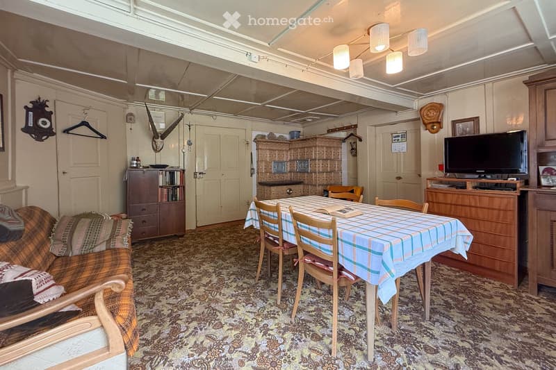 Interior with carpeted floor, dining table with chairs, couch, shelves, decorative objects, and cabinet with TV