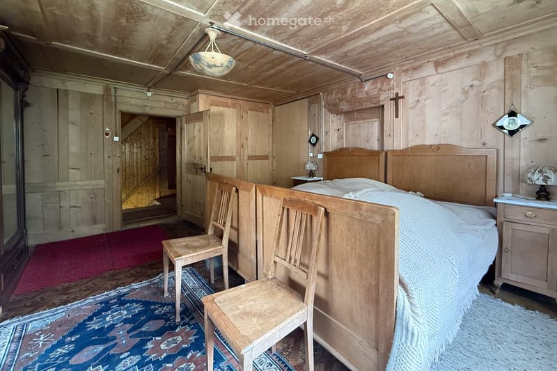 Room with wooden bed, two wooden chairs, a lamp, wooden wall and ceiling