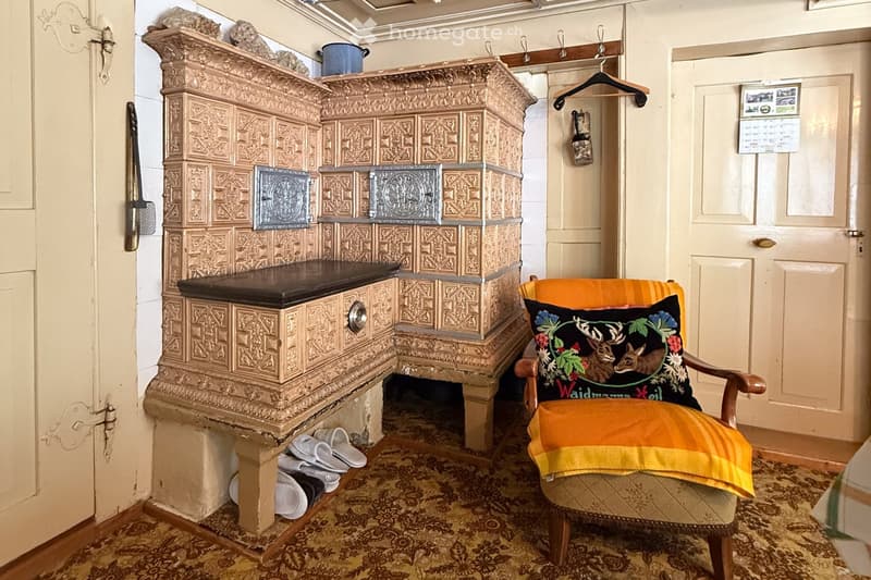 old ornate fireplace, pair of slippers under fireplace, patterned carpet, orange and yellow chair with pillow