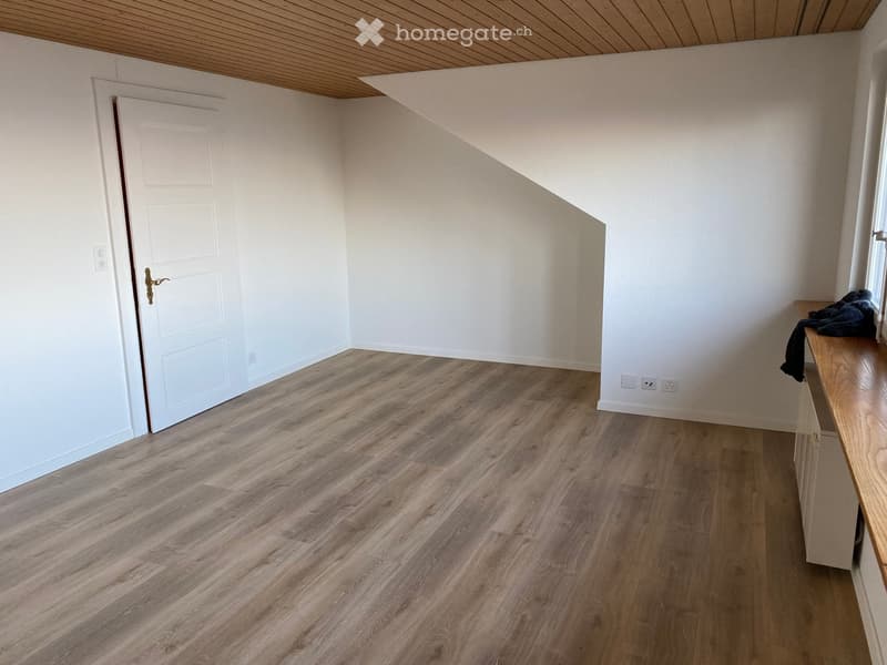 A room with wooden flooring, white walls, a door, power outlets, and cabinets with a wooden countertop. There is no view to outside.