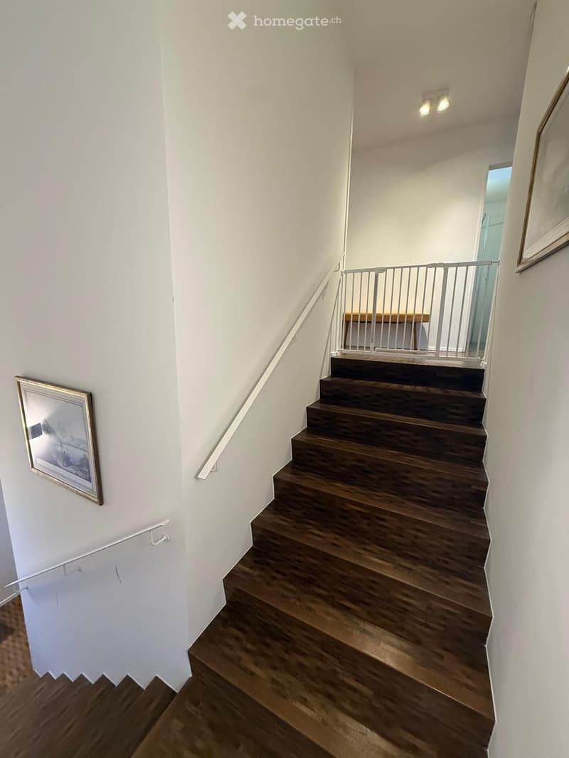 Corridor / Hallway. Wooden staircase with white walls, framed artwork, and a small landing area with a table and railing.
