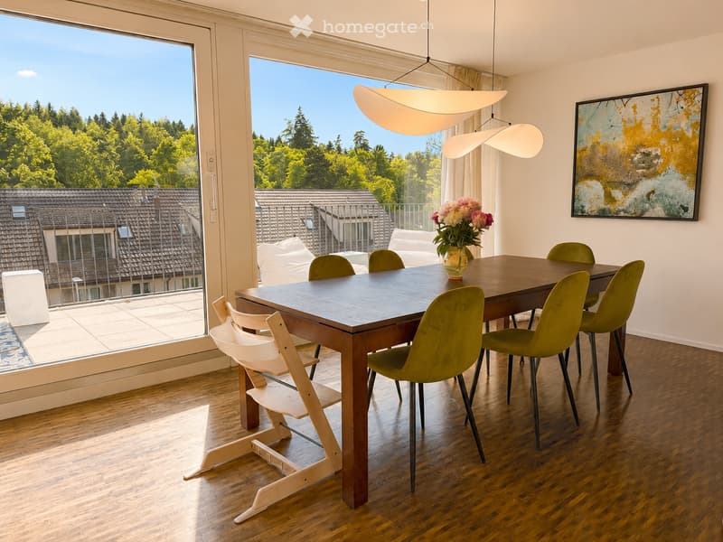 Furnished Room. Dining room with a wooden table, green chairs, a vase with flowers, and a large window offering a view of the city and trees.