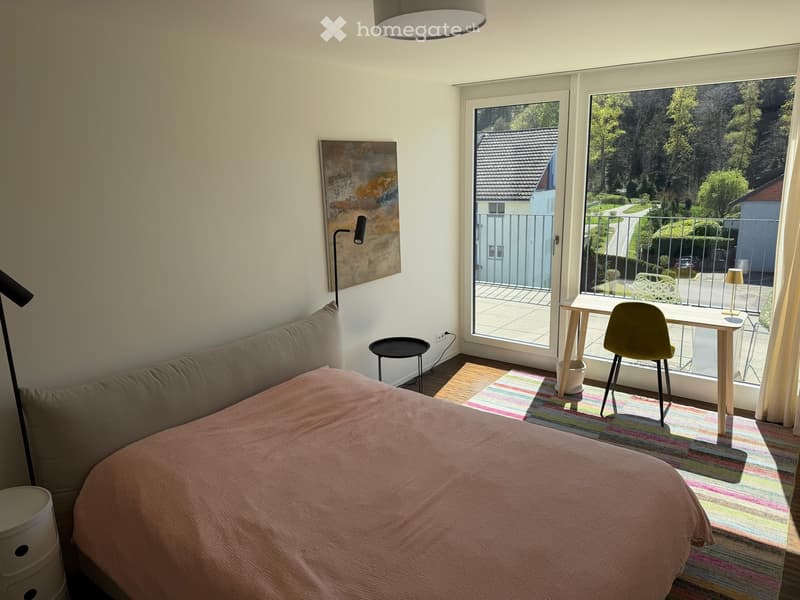 Bedroom. Bright bedroom with a bed, a small desk with a chair, a colorful rug, and a view of a garden through large windows.