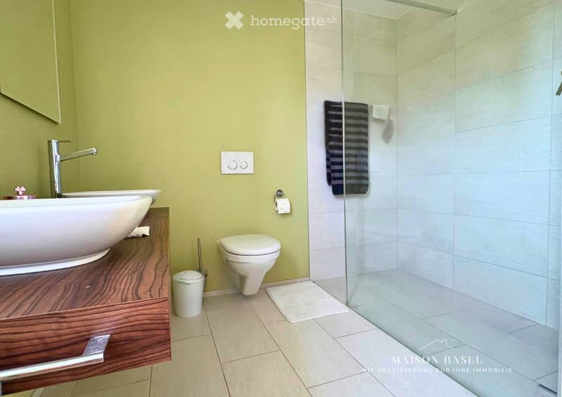 Modern bathroom with a white sink, chrome faucet, toilet, glass shower enclosure, and a towel hanging on the wall.