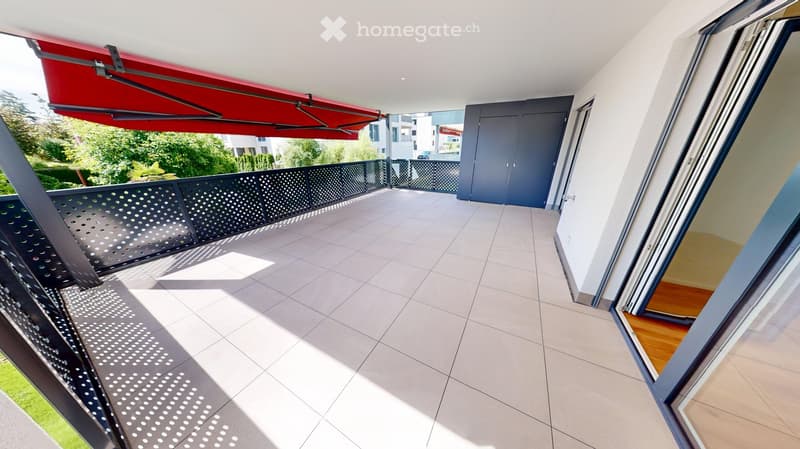 Balcony with tiled floor, metal railing, retractable awning, and sliding glass doors leading to interior.