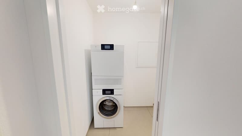 A small, clean room with a white washing machine and dryer stacked vertically, white walls, and a tiled floor.