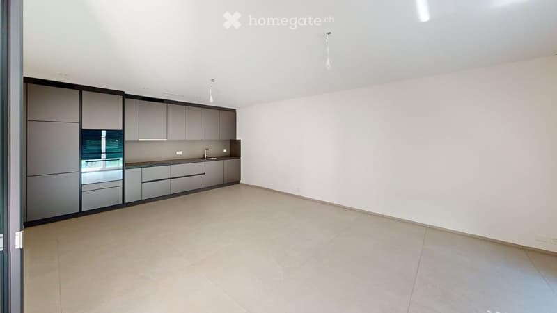 Empty kitchen with modern grey cabinets, a countertop, and a sink. The space features light-colored tiled flooring and white walls.