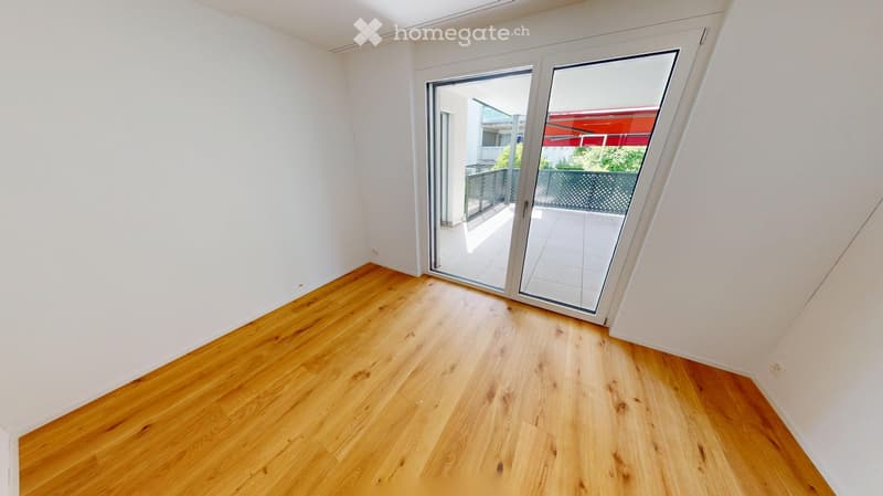 Empty room with light wooden flooring and white walls, featuring a large sliding glass door leading to a balcony.