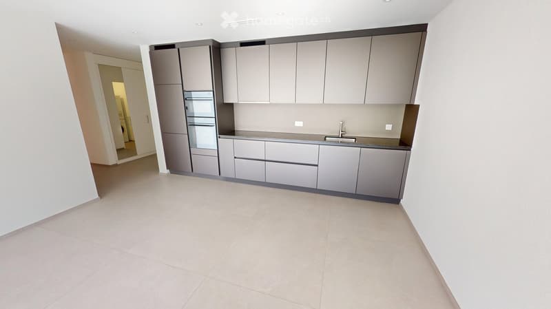 Empty kitchen with grey cabinets, a sink, and a tiled floor. The space is clean and unfurnished, with no appliances or furniture visible.