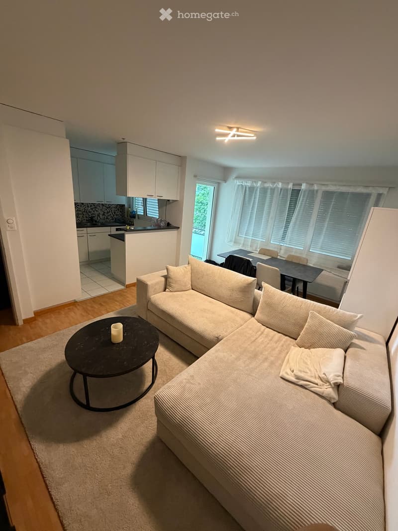 Modern living room with a sectional sofa, coffee table, dining area with chairs, and a small kitchen area.