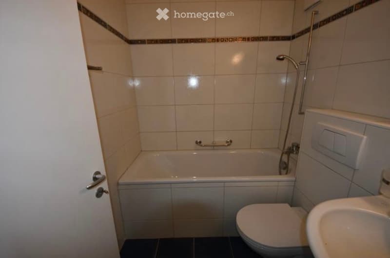 Bathroom with a bathtub, toilet, sink, and tiled walls.