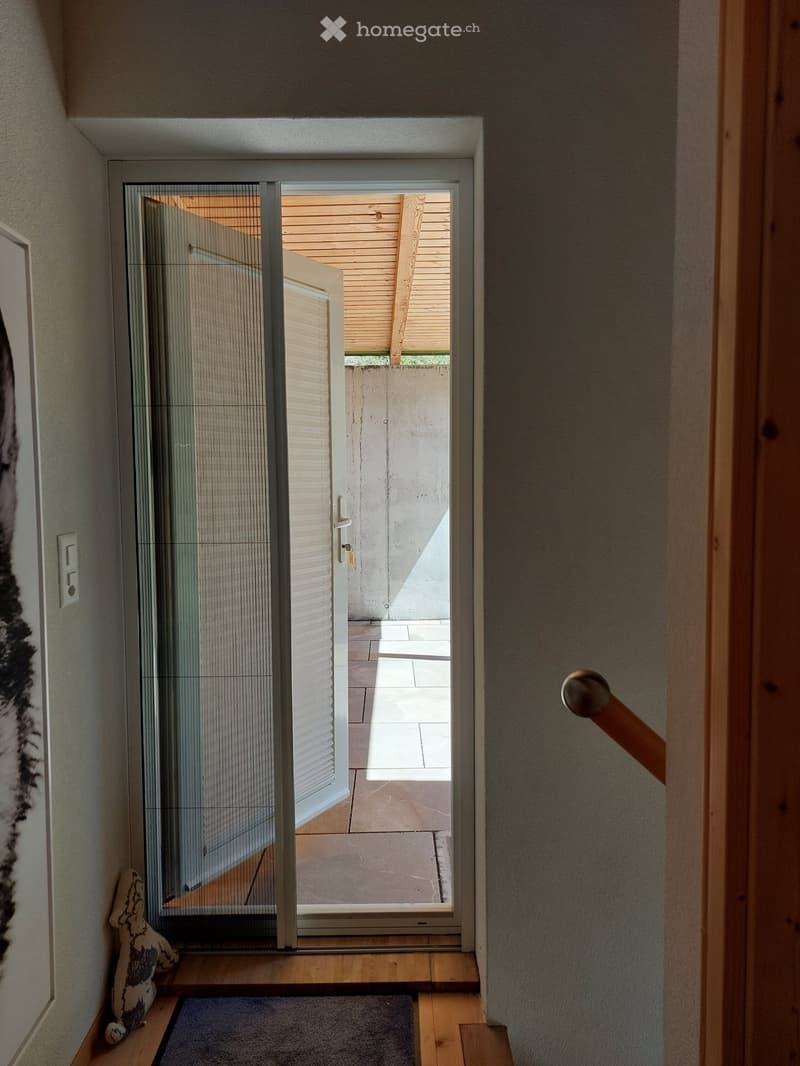 Hallway with wooden flooring, a glass sliding door leading to an outdoor area, a small bench with a decorative item, and a picture frame on the wall.