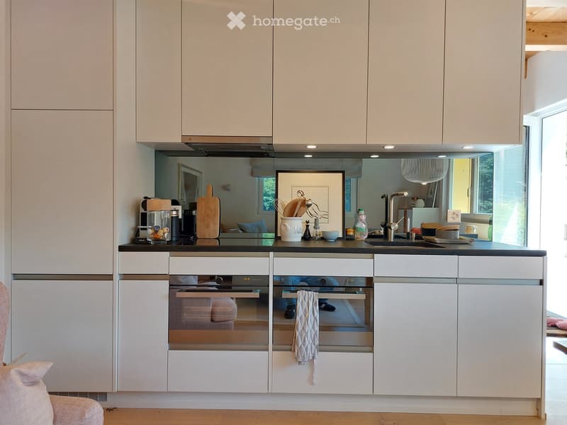 Modern kitchen with white cabinets, stainless steel appliances, and a black countertop. Features an oven, sink, and various kitchen items on the counter.