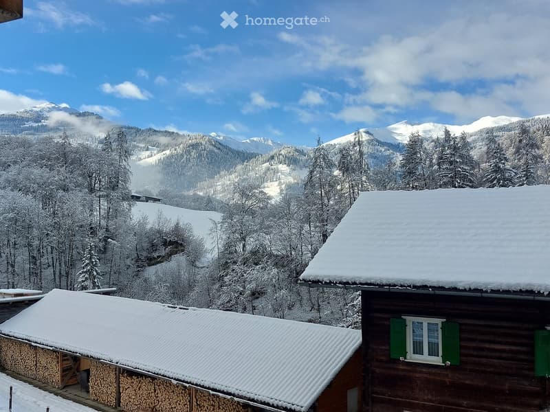 A serene snowy mountain landscape with a wooden cabin and a wood storage shed, surrounded by snow-covered trees and distant snow-capped peaks.