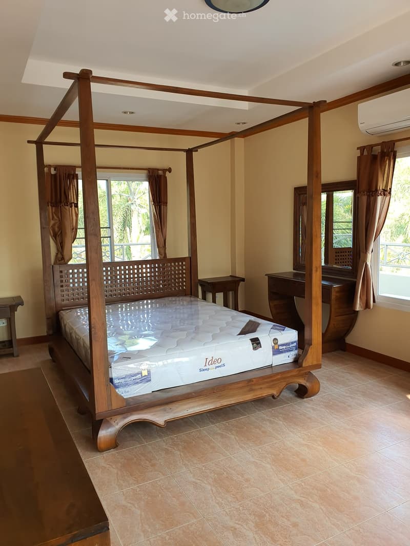 Spacious bedroom with a large wooden four-poster bed, nightstands, a desk, and large windows with curtains.