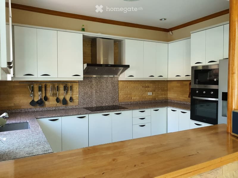 Modern kitchen with white cabinets, granite countertops, stainless steel oven, range hood, and hanging utensils.