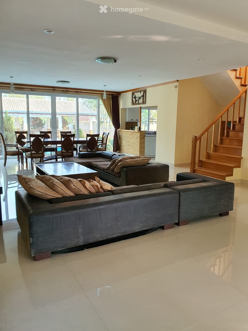 Spacious living and dining area with modern furniture, large windows, and a staircase leading to an upper level.