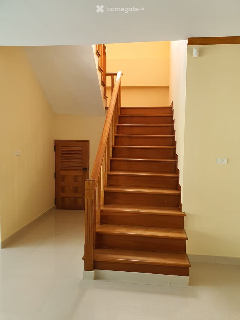 Wooden staircase with a handrail, beige walls, and a closed wooden door on the left side.