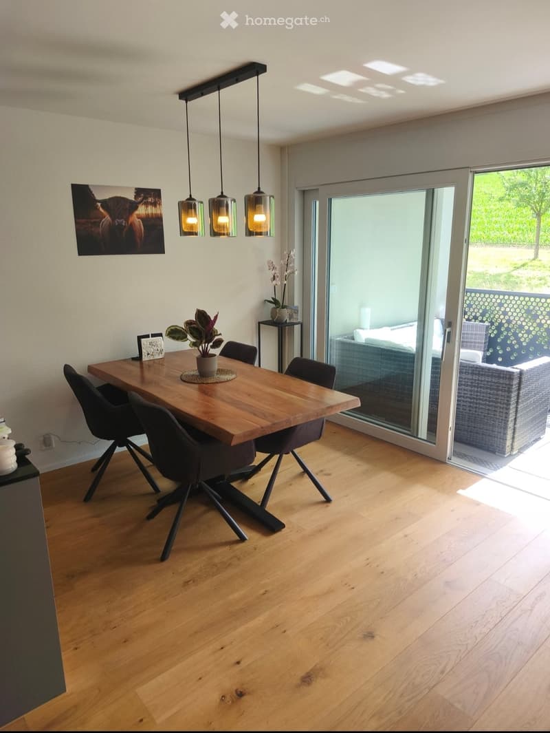 Modern dining room with wooden floor, large wooden dining table, pendant lights, and a view to the outdoor patio.