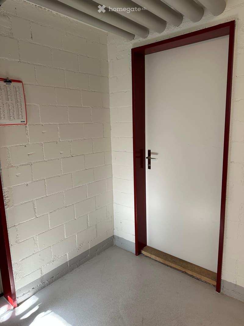 Empty hallway with white brick walls, a red-framed door, and a concrete floor.