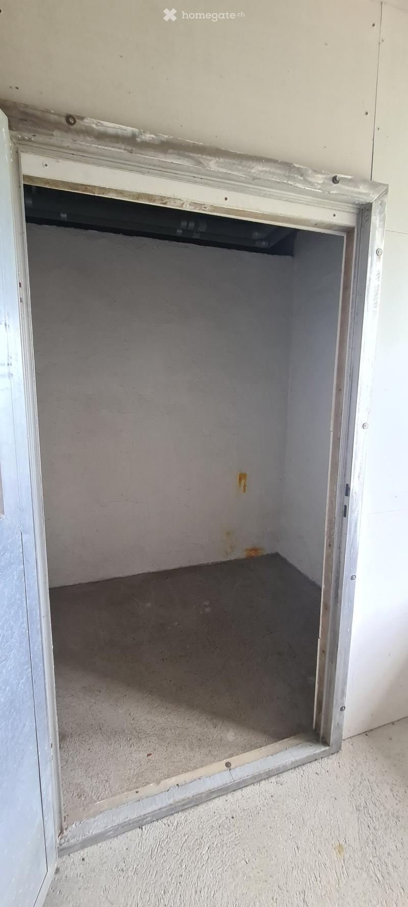 Empty room with bare walls and concrete floor, showing a doorway with a metal frame and visible construction details.