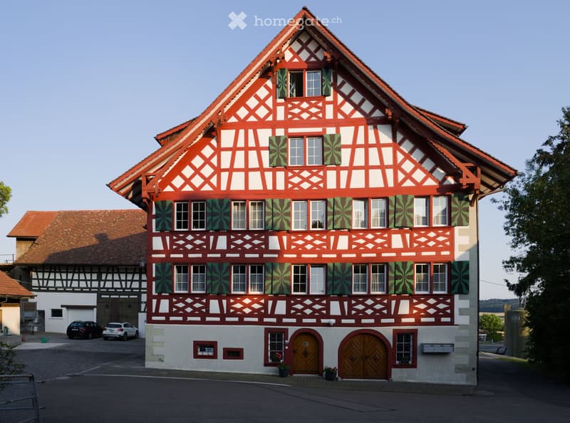 Traditional half-timbered house with red and white painted facade, green shutters, and ornate wooden doors.