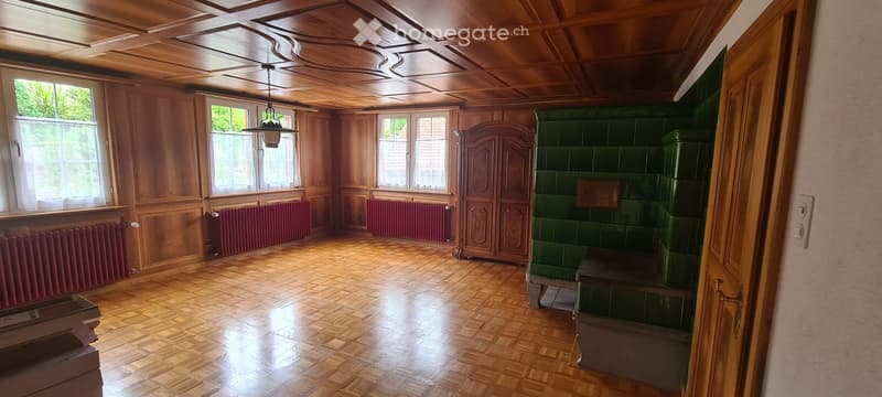 Empty room with wooden walls, ceiling, and floor, large windows, radiators, and a wooden cabinet.