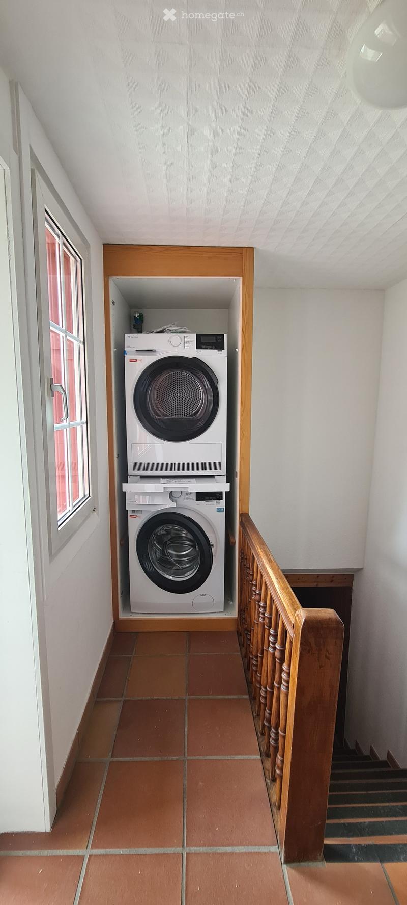 Hallway with tiled floor, wooden railing, and built-in washing machine and dryer unit.