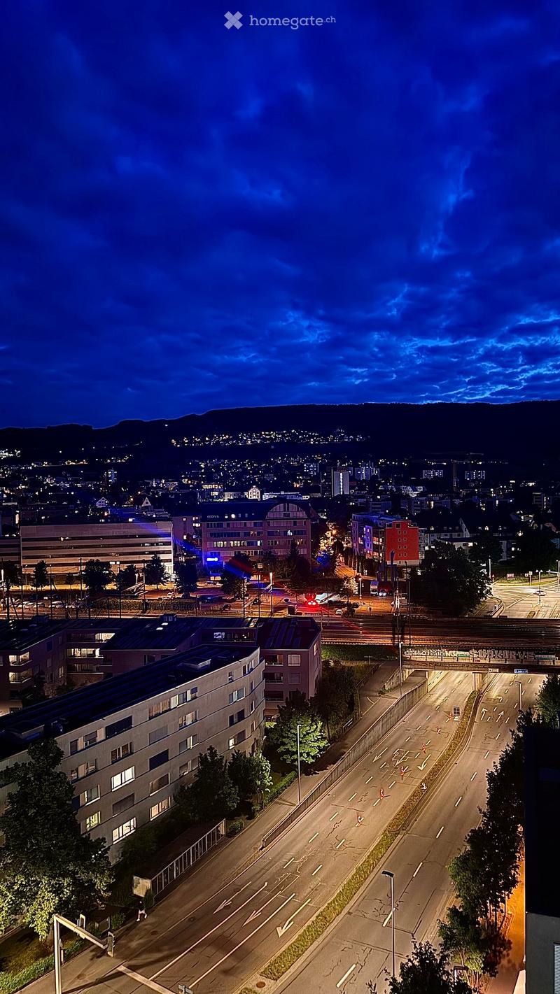 A nighttime aerial view of a cityscape with illuminated buildings, roads, and distant mountains.