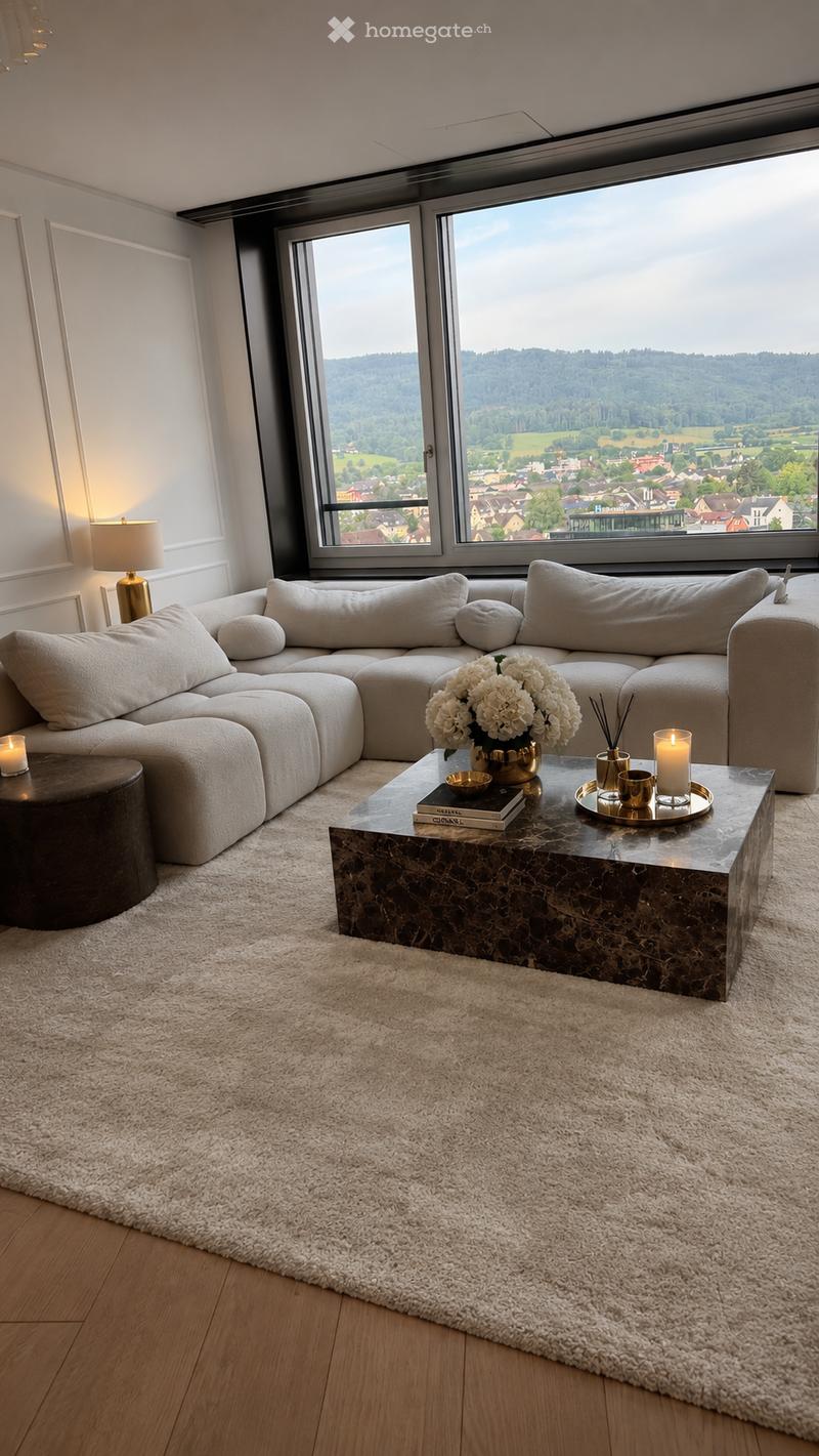 Modern living room with large windows offering a scenic view, featuring a sectional sofa, a marble coffee table, a table lamp, and decorative candles.