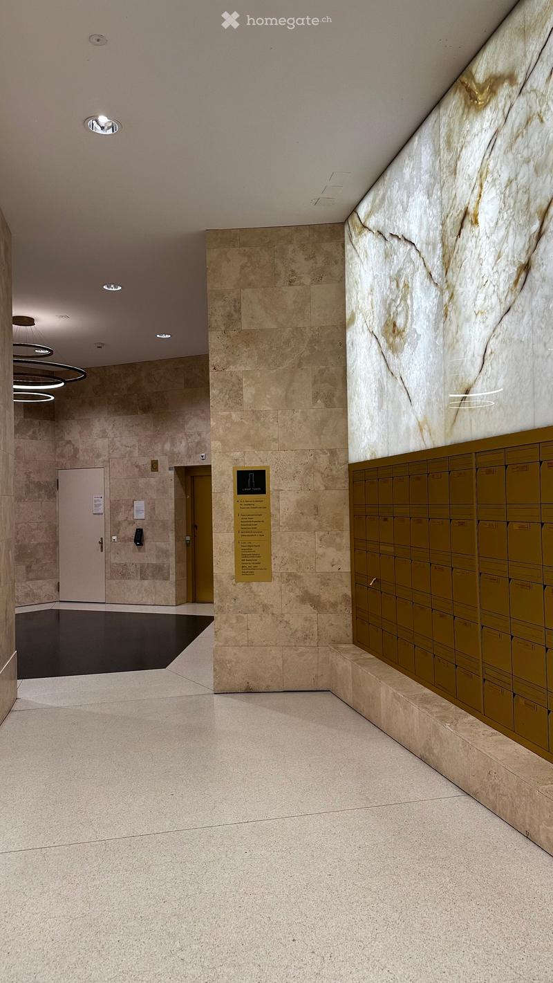 Modern hallway with marble walls, polished stone floors, and recessed lighting. Features a row of mailboxes and a signboard on the left side.