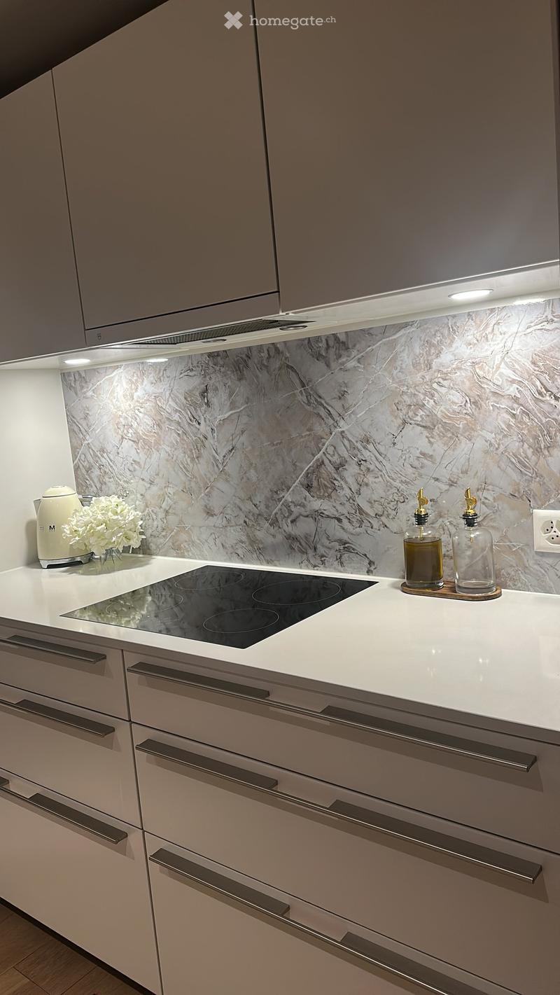Modern kitchen with white cabinets, marble backsplash, induction stove, and decorative items on the counter.