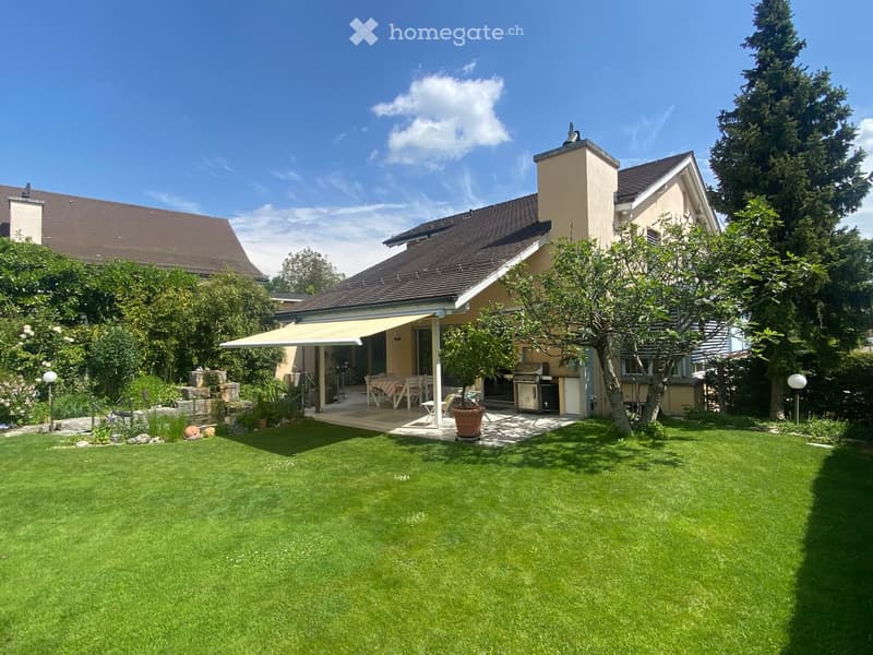 Well-maintained garden with a lawn, patio area, outdoor furniture, and a covered seating area attached to the house.