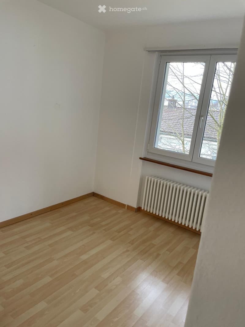 Empty room with light wooden flooring, white walls, a window with a radiator below, and a wooden sill.