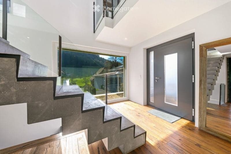 Modern hallway with wooden flooring, large window offering a scenic view, and a grey door leading to another area.