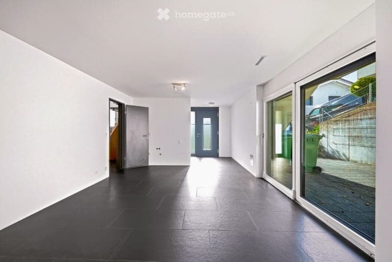 Empty hallway with white walls, black tiled floor, and large glass door leading to the outside.