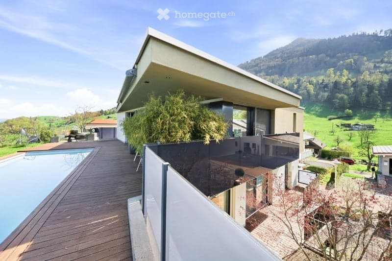 Modern two-story house with a large balcony overlooking a scenic valley, featuring a swimming pool and lush greenery.