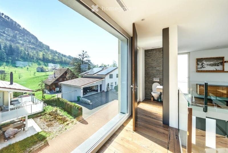Modern bathroom with wooden flooring, large window offering a scenic mountain view, toilet, and a mirror on the wall.