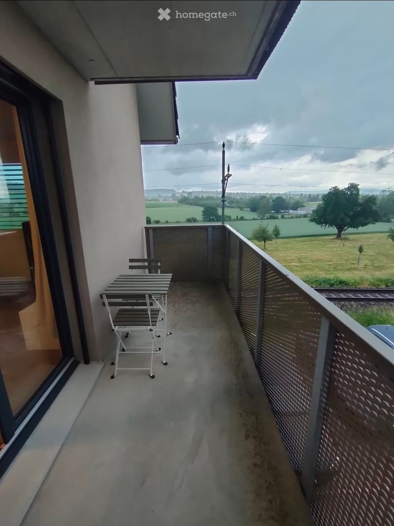 Balcony with a table and chair, overlooking a rural landscape with fields and trees.