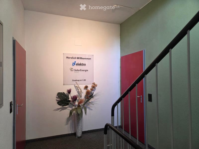 Hallway with a staircase, a vase with flowers, and a sign welcoming visitors to the first floor reception.