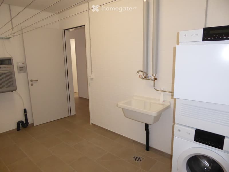 Furnished Room. Utility room with a sink, washing machine, and air conditioner. The room has tiled flooring and white walls.