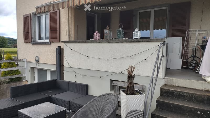 Balcony / Terrace. Balcony with wicker furniture, string lights, decorative lanterns, and a potted plant, overlooking a rural landscape.