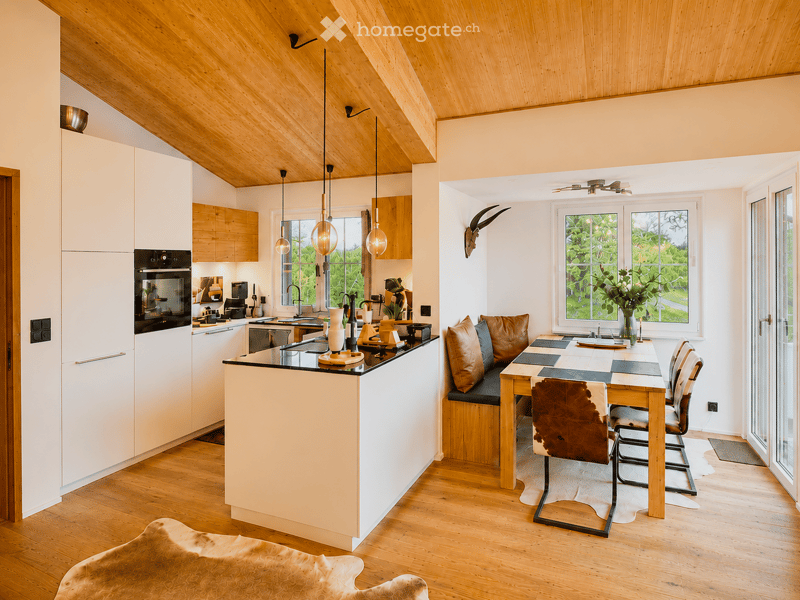 Open-plan kitchen and dining area with white cabinets, wooden ceiling, pendant lights, and a dining table with chairs.